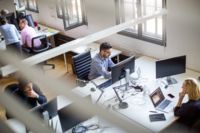 CANCOM Austria employees sit at a shared desk and work on laptops.